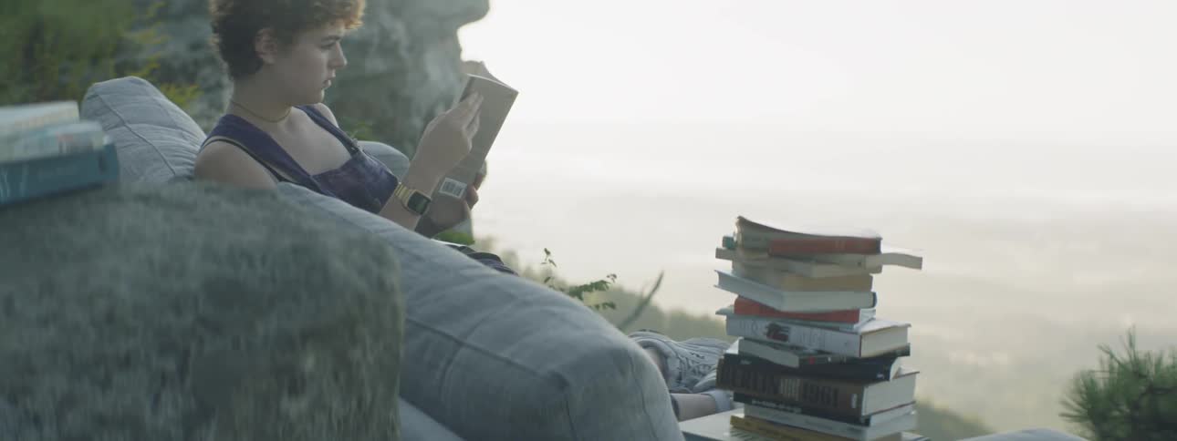A woman reads books on a couch outdoors