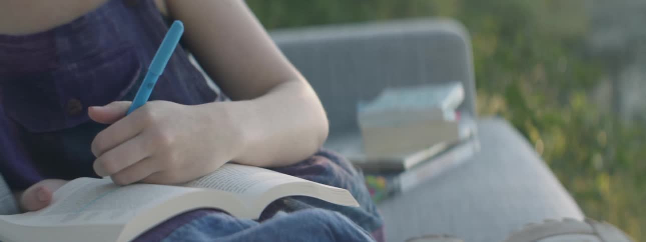 A woman reads books on a couch outdoors