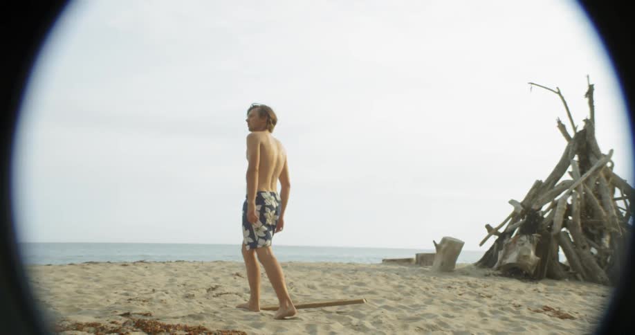 A man walks on the beach near a wood tent
