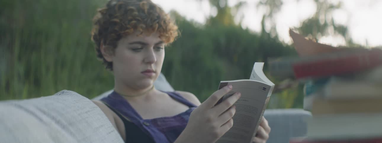 A woman reads a book on a sofa outside