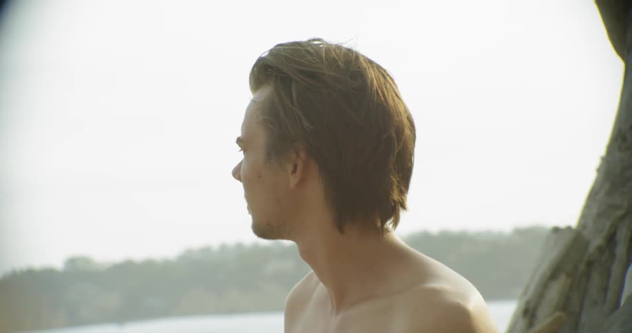 A shirtless man stands outside on a sunny day