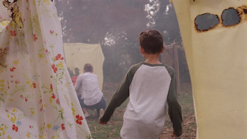 A child sneaks up on a woman hanging clothes in the yard