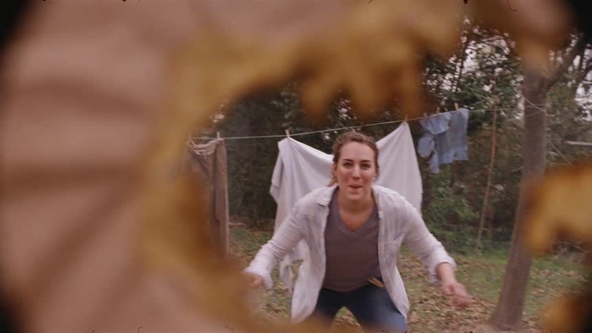 Woman turns and runs through the clothes on a clothesline