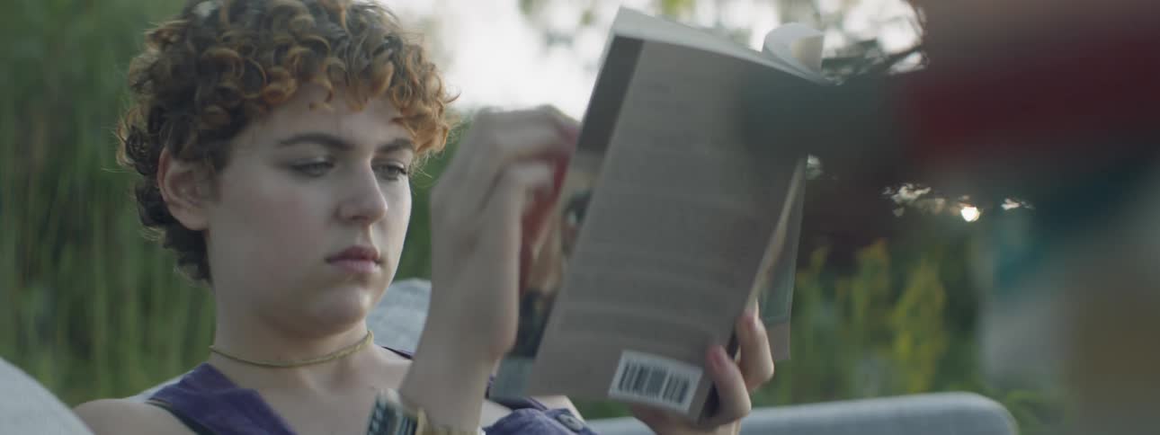 A woman is sitting outside in daylight reading a book