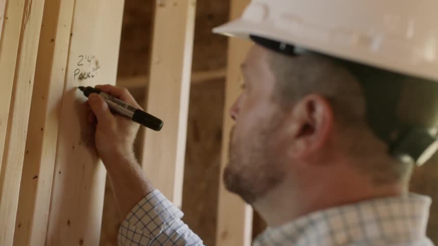 Man wearing a hard hat draws on a wooden beam