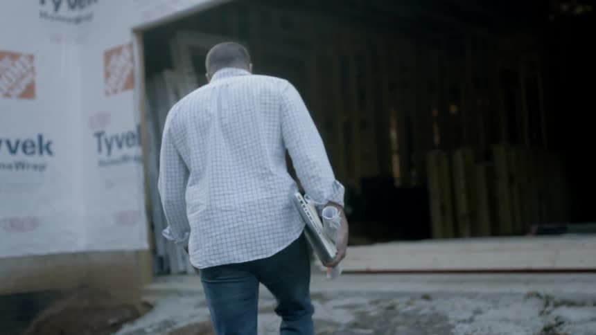 A man carrying blueprints is walking towards a construction project in daylight