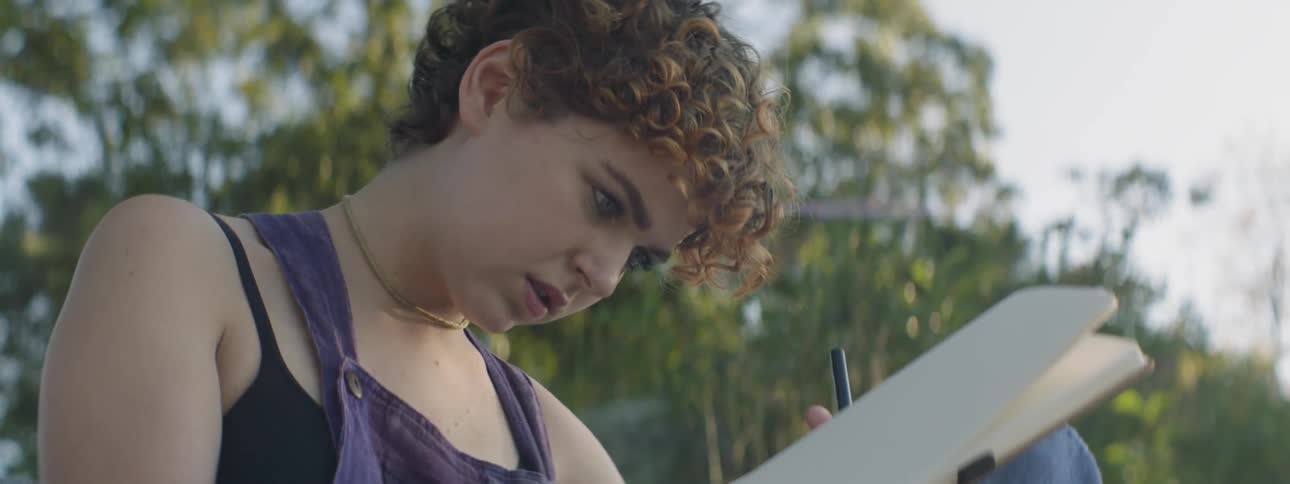 A girl is writing in a notebook as she sits outside on a sunny day