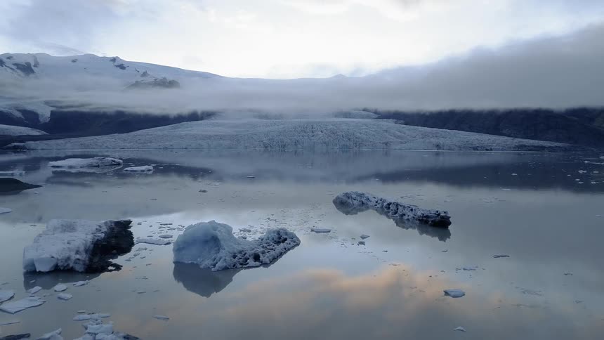 Clouds are hanging over a glacier and icebergs at dawn