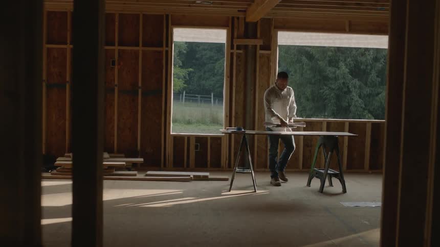 Man walks into an empty room with rolls of paper and puts them on a workbench