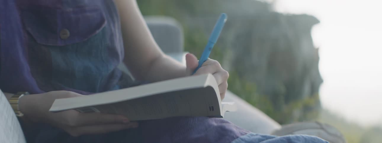 A woman writes in a book on a sofa outside
