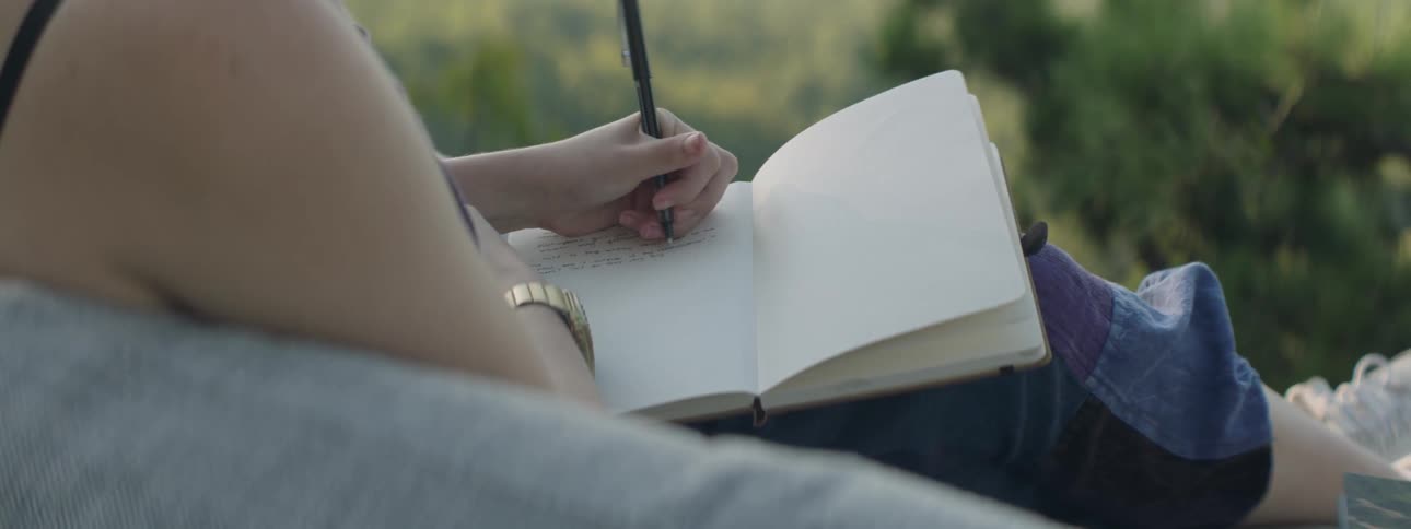 A woman journals on a sofa outside
