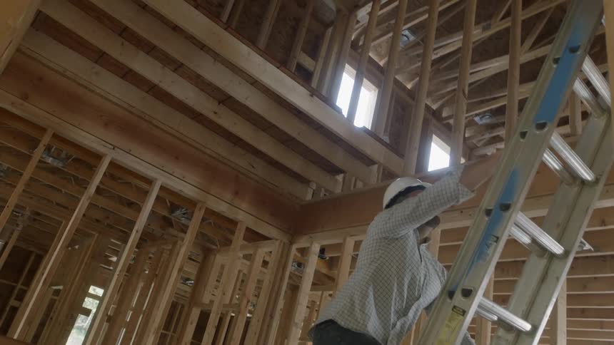 Man wearing a safety hat climbs a ladder in a building under construction