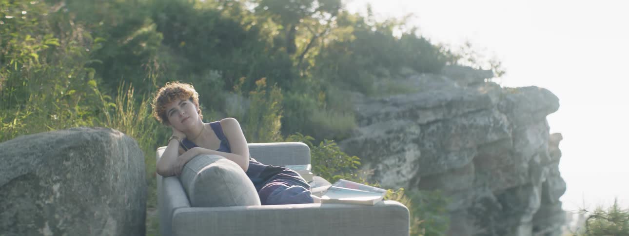 A woman is sitting outside on a couch daydreaming in sunlight