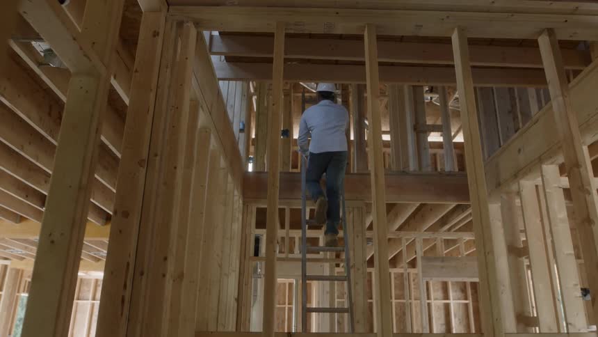A man in a hard hat climbs up on a construction site