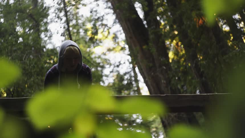 A woman leans over a wooden railing in a forest