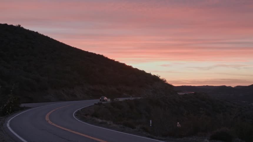 Vehicles driving down a winding mountain road at sunset