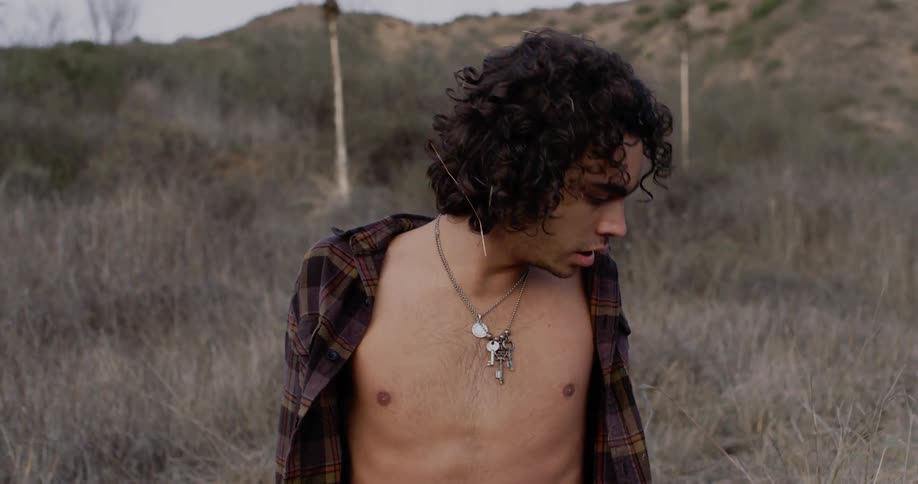 Man wearing keys on a chain breathes heavily as he sits in a field