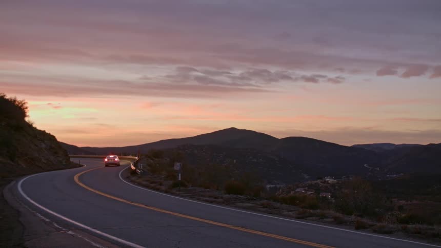 A car driving down a winding mountain road as the sun sets