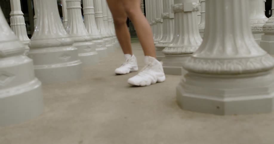 The woman is dancing past the white pillars