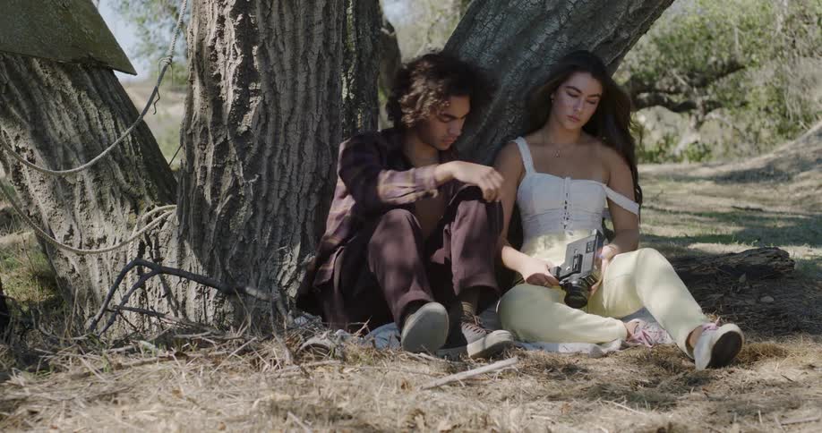 A man and woman sit down leaning against a tree
