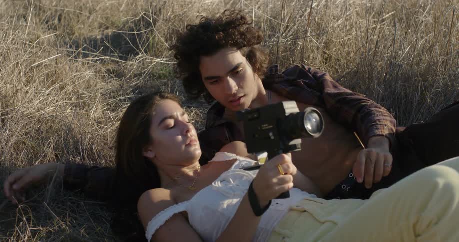 Woman holds a video camera as she lays in a field with a man