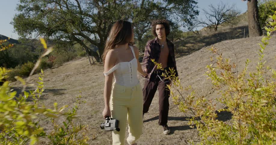 Woman holds a camera as she walks with a man in the field