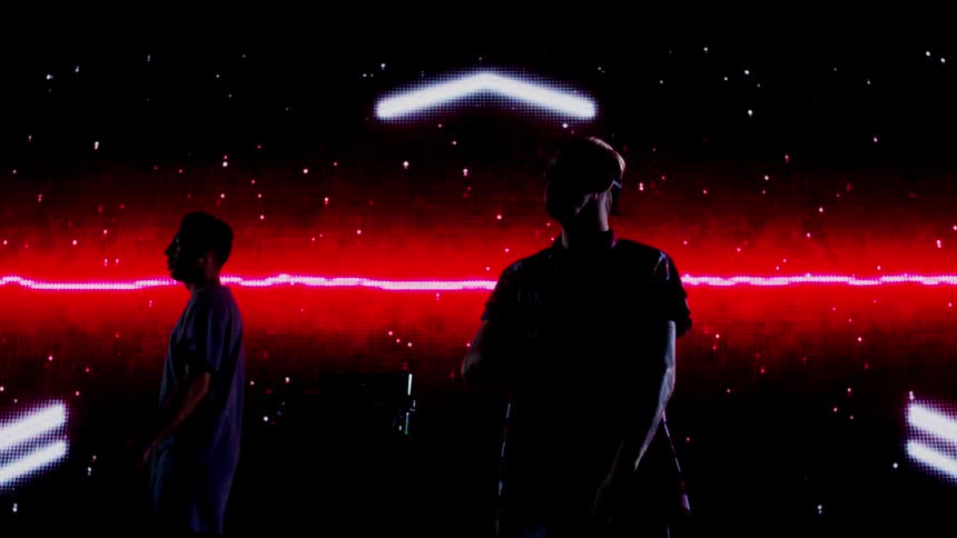 Two djs perform in front of a projection screen