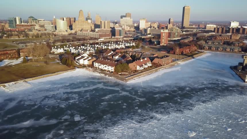 Ice is covering a waterway near a city on a sunny day