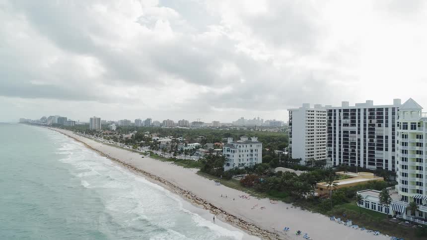 Waves are rolling onto a beach in a resort area on a cloudy day