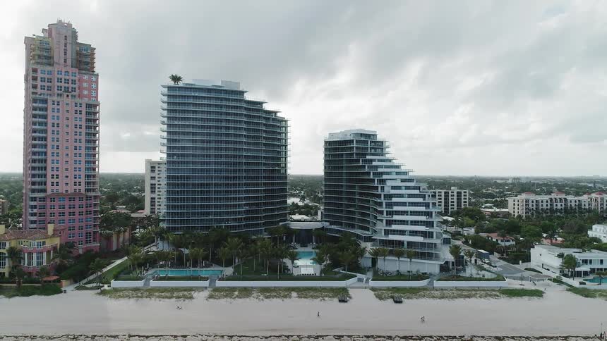 People walk on a beach beyond high rise hotels on a cloudy day