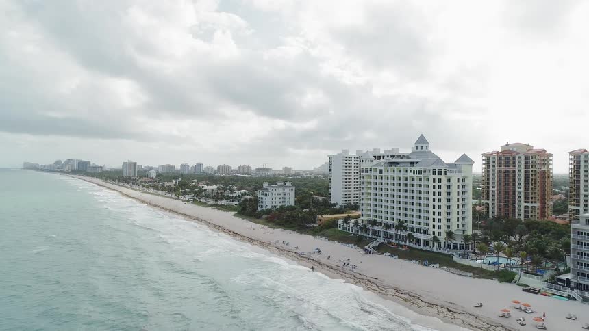 Waves are rolling onto a beach in a resort area on a cloudy day