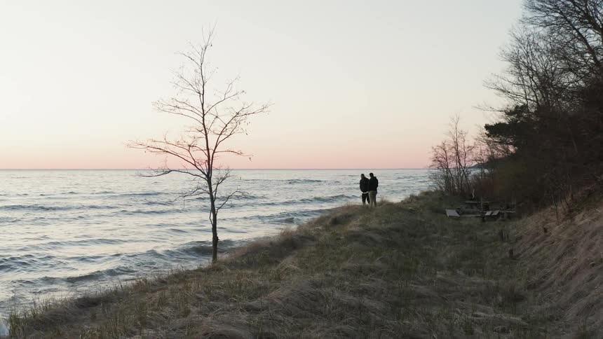 Two people stand on a hill and look out at the lake