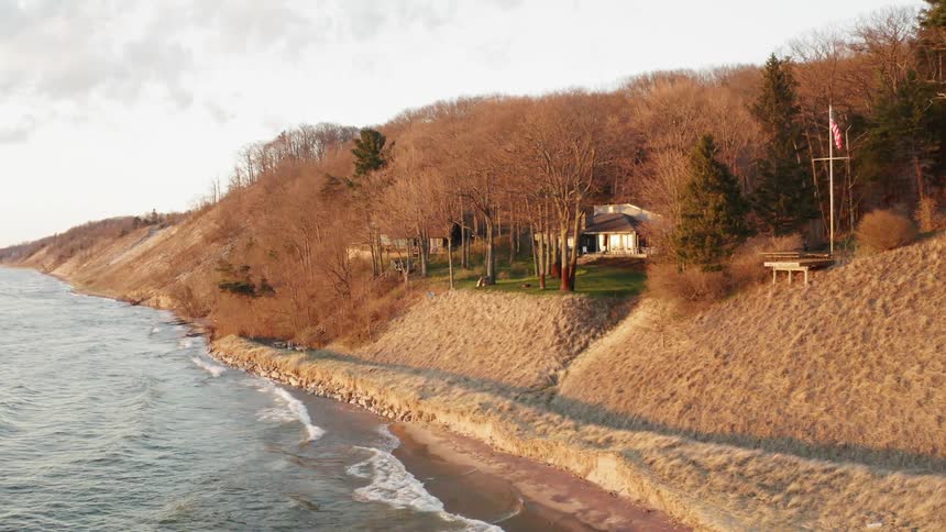 Waves are rolling onto a beach near a house on a cloudy day