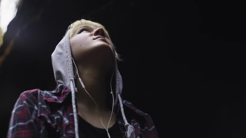 A woman with earbuds stares upwards