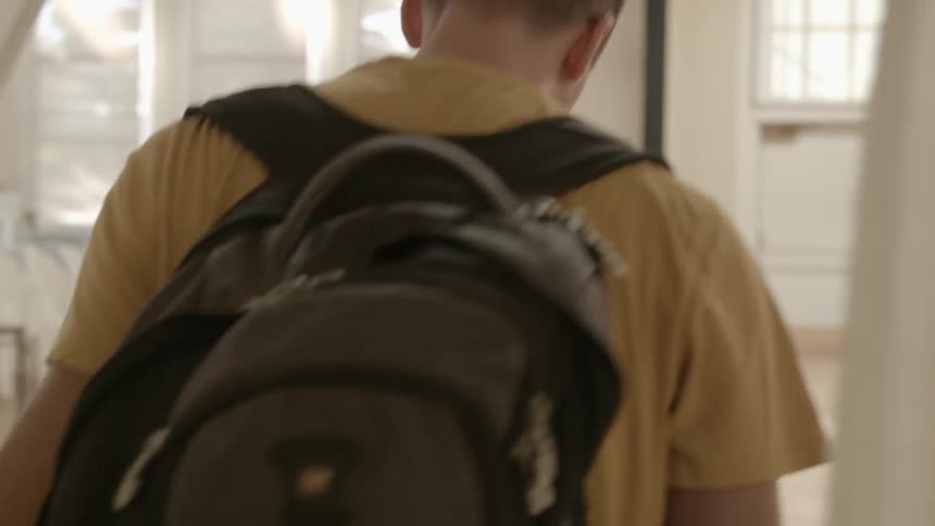 Young man walking through doorway wearing a backpack