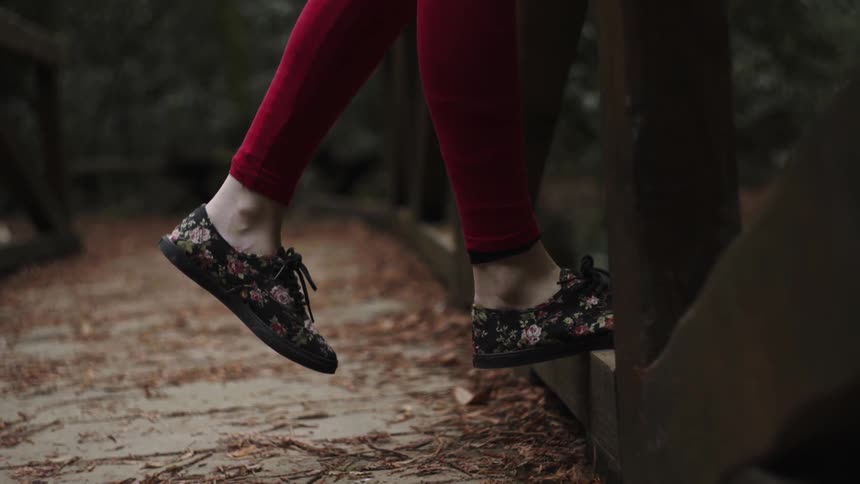 Female legs with red colored leggings and flowery flat shoes stepping on a bridge railing