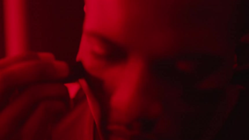 A football player in uniform applies eye black in a red light