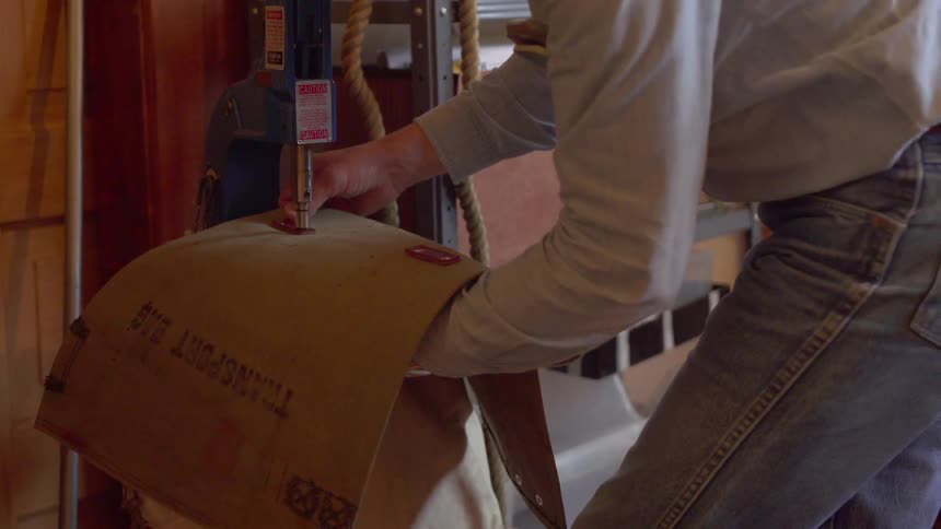 A man uses a tool to apply a fastener to leather