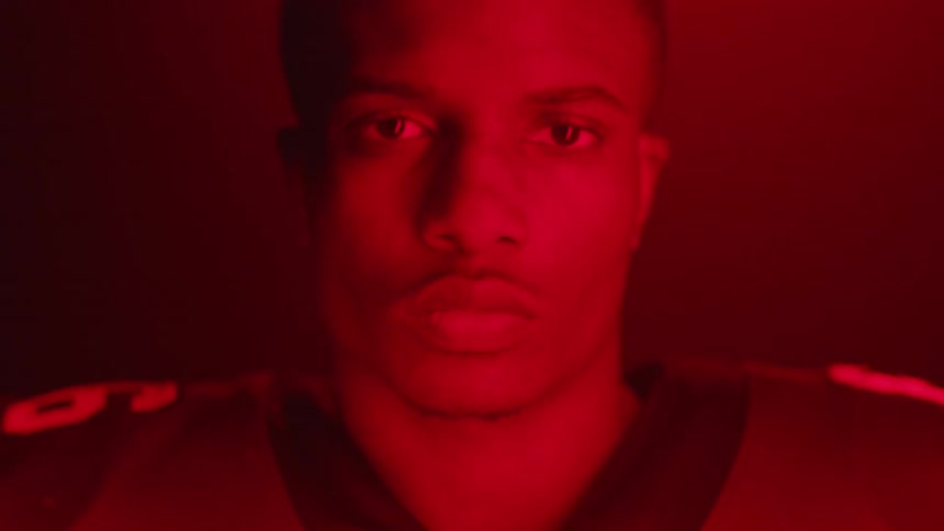 Football player puts on helmet in room with flashing red lights