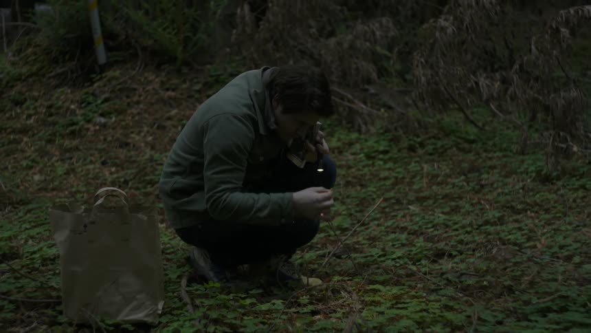 A man shines a flashlight on an object in the woods