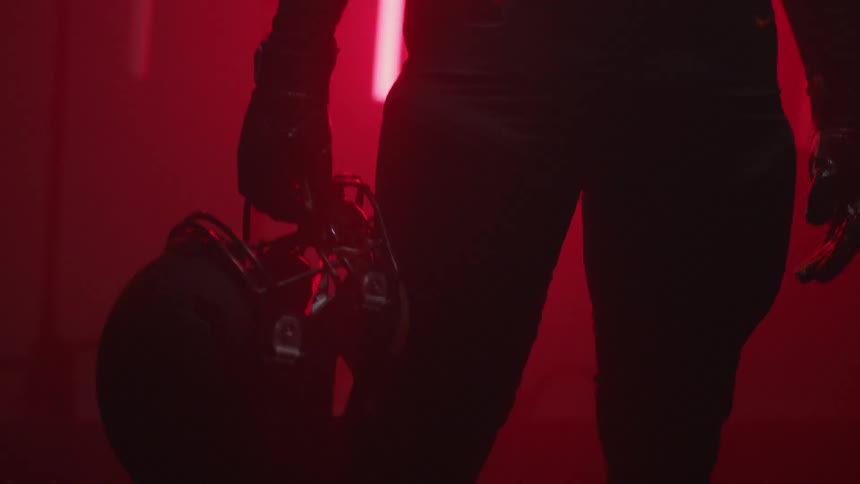 Man in football jersey is holding helmet in room with red flashing lights