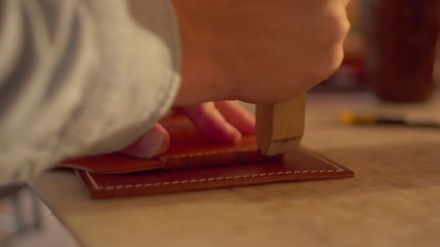 A man uses a wooden hand tool to smooth stitched leather