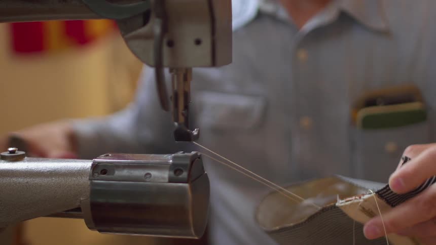 Man sews striped fabric and cuts thread with red scissors