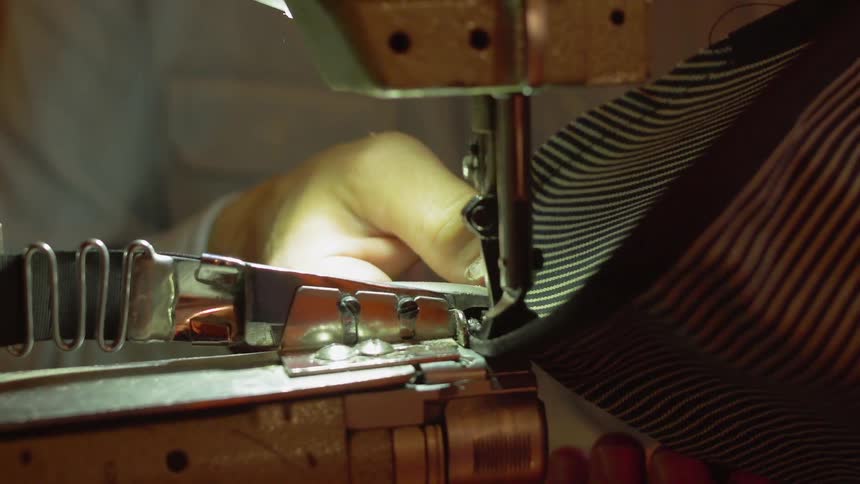 A man is sewing material on a sewing machine during daylight