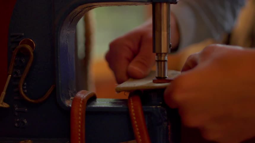 Man uses a tool to stamp a hole in leather