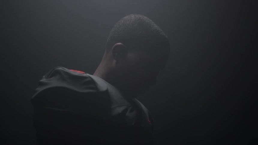 A football player is standing in a dark room with his head inclined down