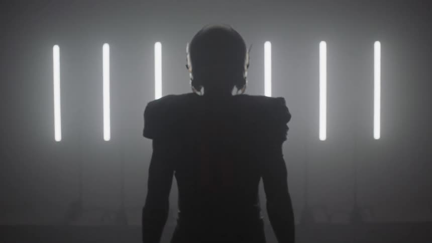 Person wearing football gear stands in a dark room with lights flashing