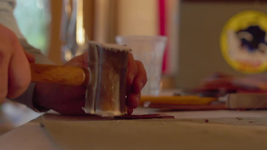 Person uses a hammer and chisel to pound on a small piece of wood