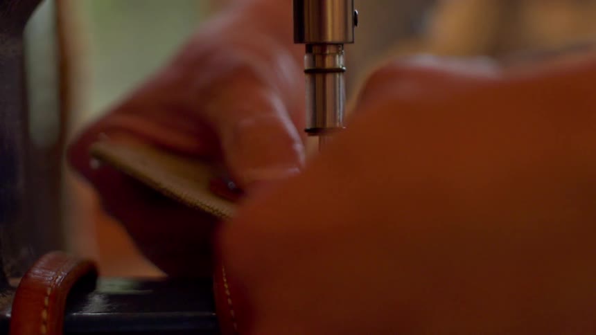 The person feeds leather through the machine
