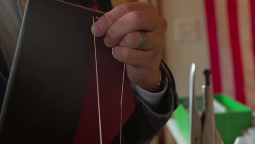 Man pulls string through holes in a piece of leather